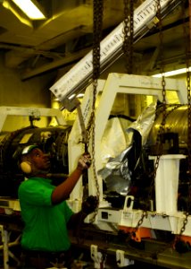 US Navy 100920-N-1092P-027 Aviation Machinist's Mate Airman William Mitchell uses a chain-fall to guide a crane while moving an F-A-18C Hornet jet