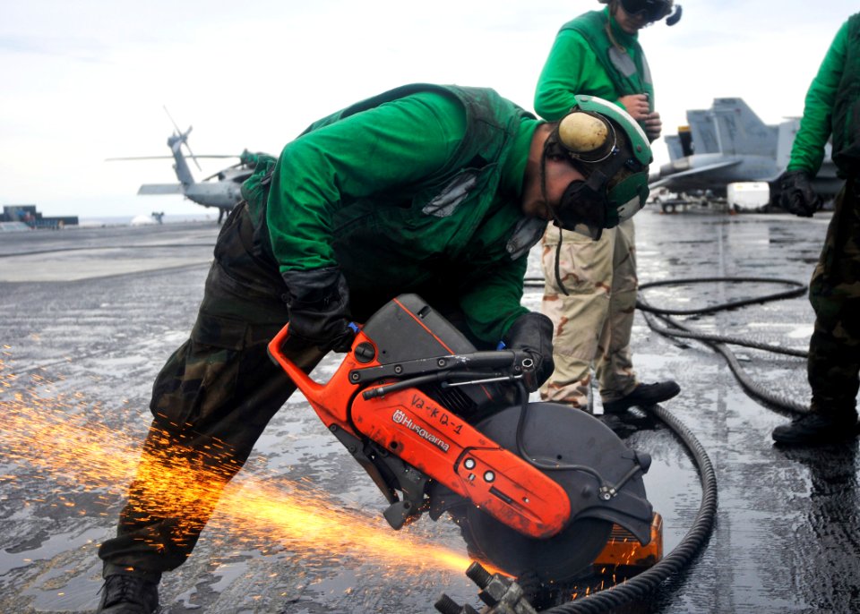 US Navy 100922-N-7103C-091 Aviation Boatswain's Mate 3rd Class Max Torres, from Houston, uses a chop saw to cut through a worn arresting cable in p