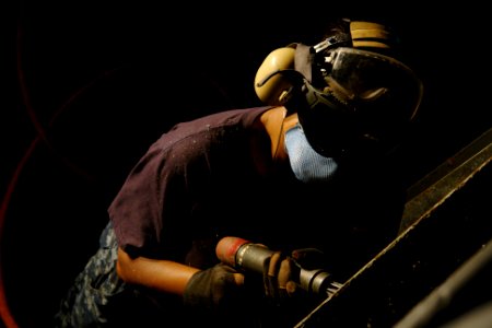 US Navy 100930-N-9643K-024 Boatswain's Mate Seaman K.L. Sams uses a needle gun to remove rust on the vehicle ramp to the hangar bay aboard the amp