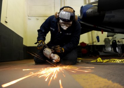 US Navy 101003-N-6427M-073 Aviation Boatswain's Mate (Handling) Airman Juan Jauregui, from New York, grinds paint off hangar bay door tracks aboard