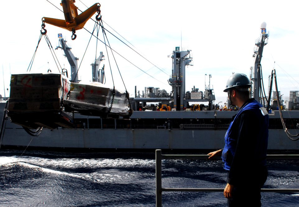US Navy 101008-N-2218S-040 Religious Program Specialist Seaman Jon Thums watches as pallets of supplies are sent from the Military Sealift Command