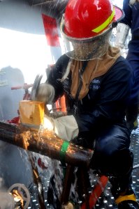US Navy 101011-N-7293M-378 Damage Controlman Fireman Kyle Lobb hammers a wooden wedge and oakum material into a gash in a training pipe