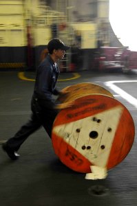 US Navy 101015-N-7605J-056 Boatswain's Mate 2nd Class Alexander Luna transports a spool during a cargo onload in the hangar bay of the aircraft car