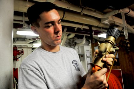 US Navy 101013-N-2953W-775 Aviation Boatswain's Mate (Equipment) Airman Patrick Fairbairn shines the vari-nozzle on a fire hose aboard the aircraft
