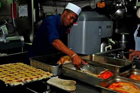 US Navy 111124-N-ER662-039 Culinary Specialist Seaman Odayne Samuels removes turkeys from an oven tray in preparation to be sliced and served for T