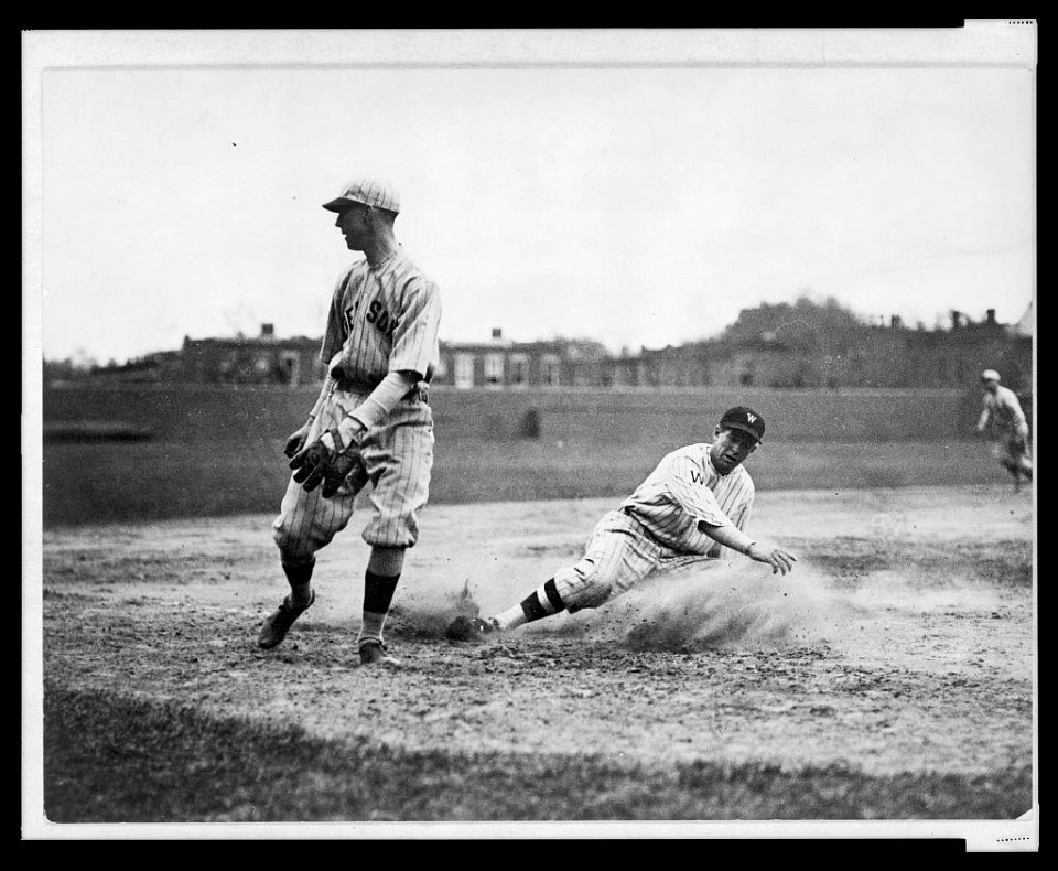 Washington Senators' Bucky Harris sliding, as he successfully steals third base in the 7th inning of a baseball game against the Boston Red Sox; third baseman Joe Dugan watches the ball roll LCCN2005676974