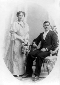 Wedding picture, man seated and woman holding flowers and standing LCCN2003681234 photo