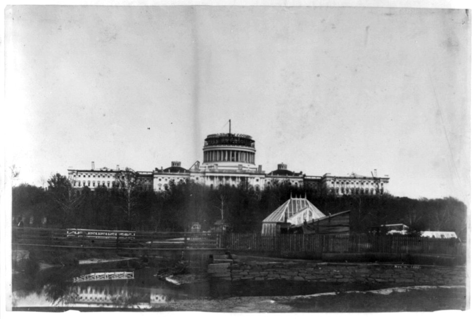 West front of the United States Capitol, with the new cast-iron dome under construction. In the foregrd. is the Tiber Creek or Washington City Canal and the octagonal greenhouse for the LCCN2002709520