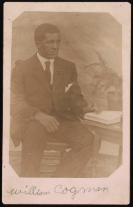 William Cogman, seated, with pen in hand writing in a book LCCN2015650011