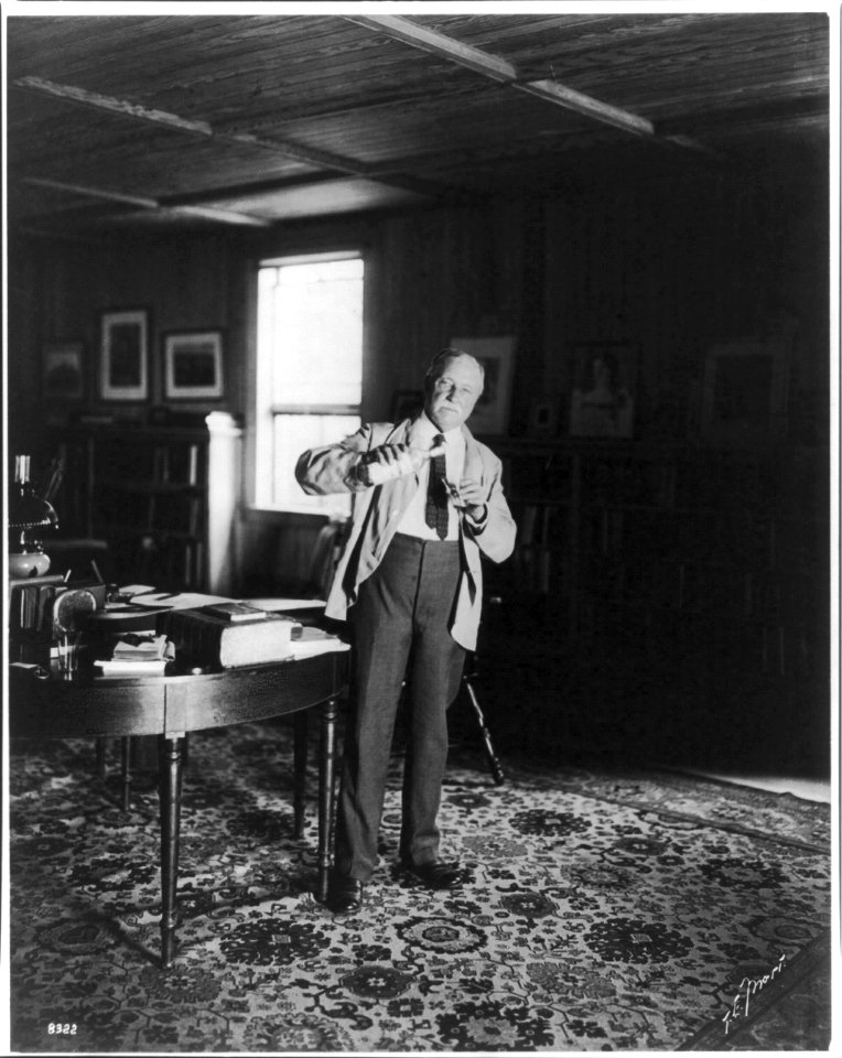 William Dean Howells, 1837-1920, full-length portrait, standing, facing right, holding bottle and glass LCCN2005691569
