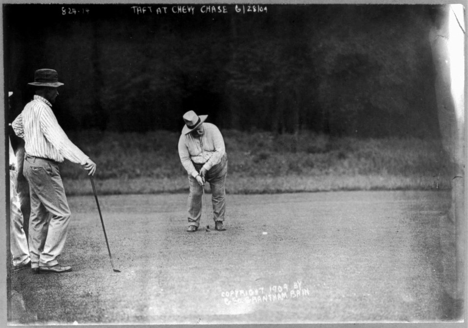 William H. Taft, full length, facing slightly left, bending over to hit golf ball, with two men on green at Chevy Chase, June 28, 1909 LCCN2005697047