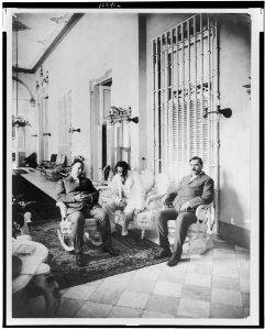 William Howard Taft, full-length portrait, seated on rocking chair, facing right, with two other men LCCN99400591