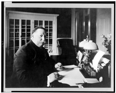William Howard Taft, half-length portrait, seated at desk, facing right, with pen and eyeglasses in his hands LCCN98515879