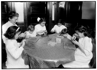 Woman and children around a table making chains for handbags LOC nclc.05504