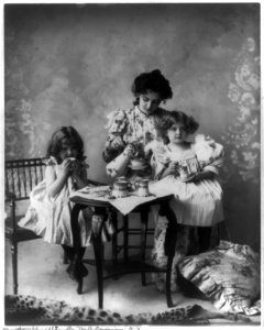 Woman and 2 girls seated at small table with cups, pitcher, etc. LCCN2002709448