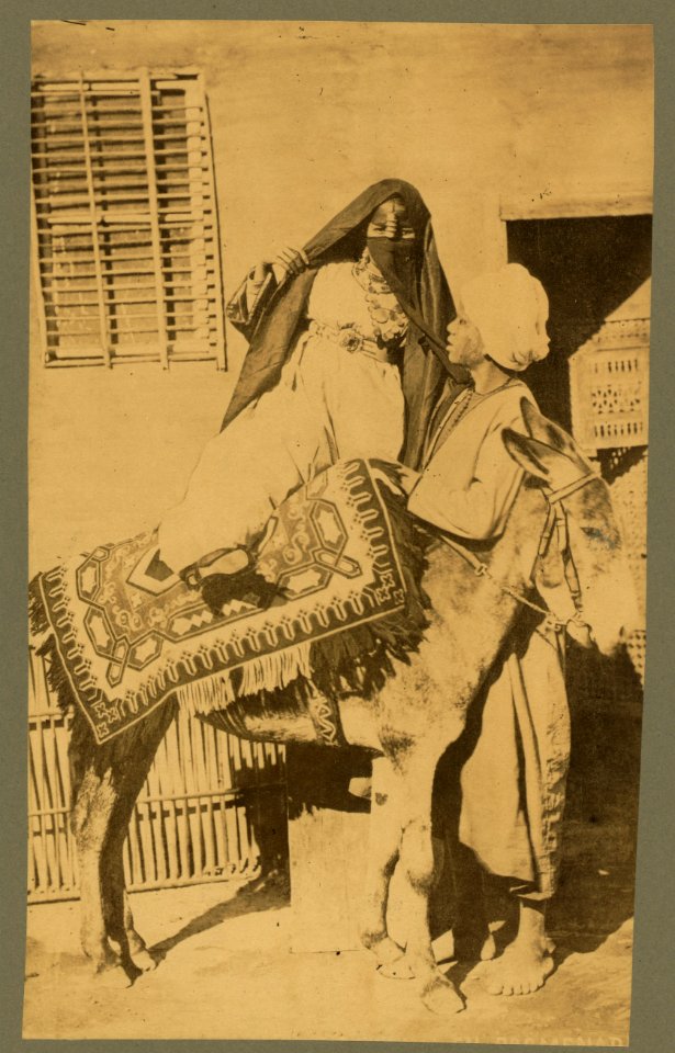 Woman assisted by man as she mounts or dismounts a donkey in Alexandria, Egypt LCCN2004671966