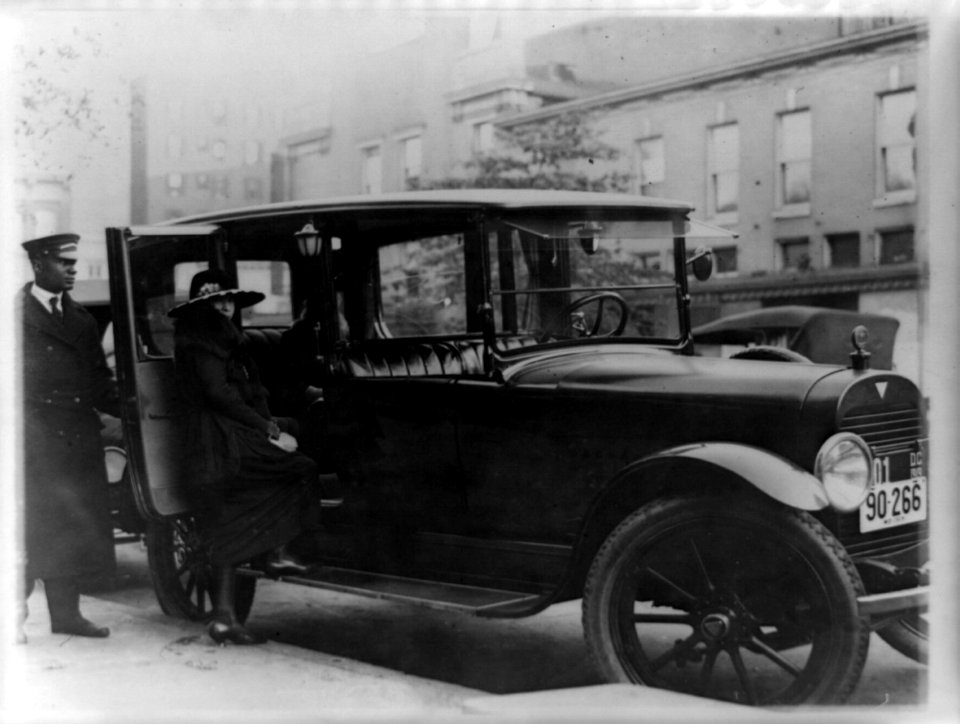 Woman getting into back seat of car as chauffeur holds door, Washington, D.C., area LCCN89713494