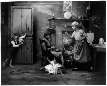 Woman holding up spoon at boy, with mask, who is scaring young girl; African American woman peeling potatoes LCCN2003675177