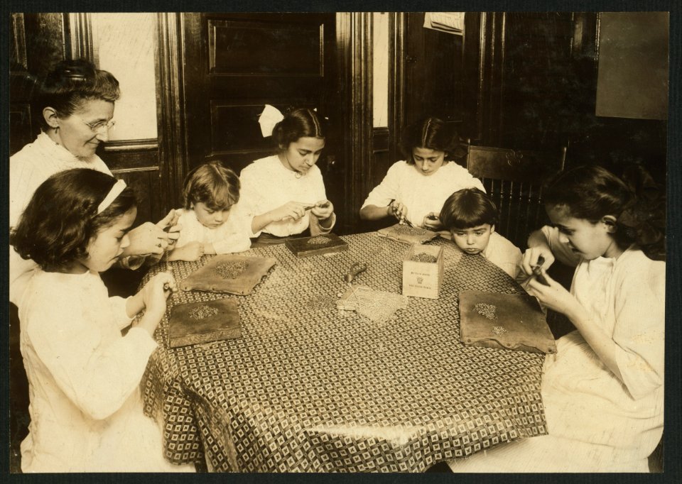 Woman and children around a table making chains for handbags LOC nclc.05504