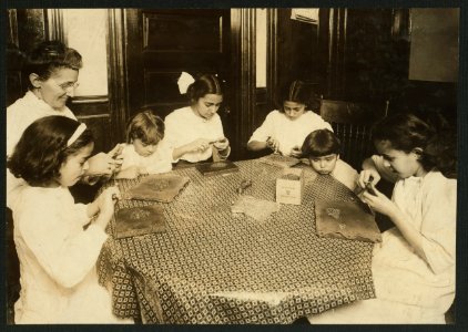 Woman and children around a table making chains for handbags LOC nclc.05504