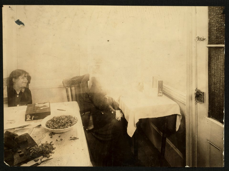Woman making Turkish Trophy cigarette cases in the kitchen of her East Side Tenement home. Food Scattered about on the table. The door on right is the toilet. (For complete details see Miss LOC nclc.04267
