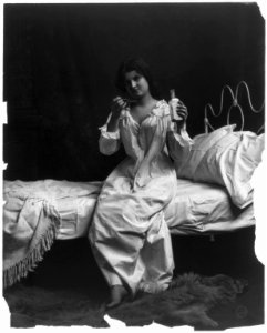 Woman seated on bed and taking spoonful of medicine LCCN2002699163