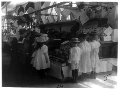 Woman schoolteacher and group of young pupils examining fruits and vegetables at a market on field trip. Washington, D.C. 5th Division LCCN2001703690