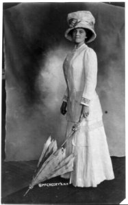 Woman wearing foot-lgth. dress and hat and holding umbrella with tip on floor. LCCN2002697733