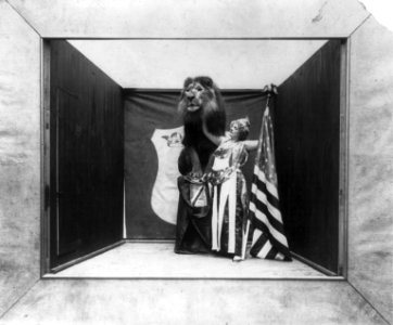 Woman with stars and eagle on her costume holding U.S. flag and touching tame lion under its neck LCCN2002711737