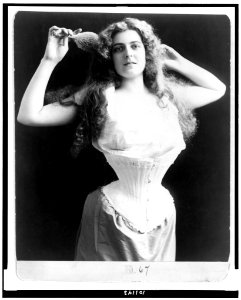 Woman wearing corset, brushing her hair, half-length portrait, standing, facing front LCCN90710046
