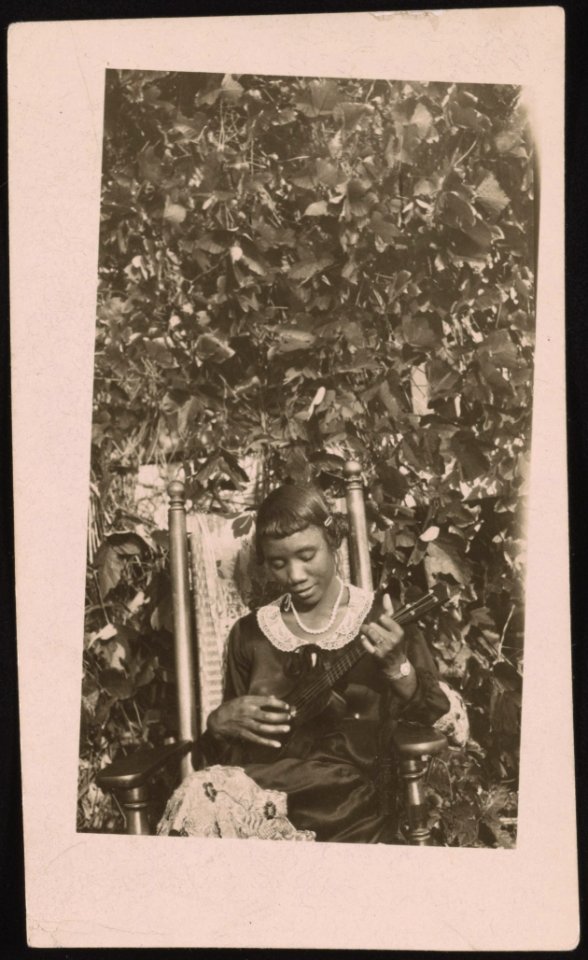 Woman, seated, playing ukulele, vines in the background LCCN2015650137