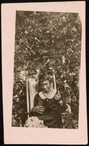 Woman, seated, playing ukulele, vines in the background LCCN2015650137