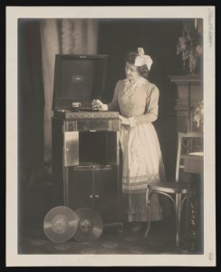 Woman, with large bow in her hair, putting needle on record on phonograph LCCN96514245