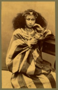 Woman, three-quarter length portrait, seated, facing front, wearing elaborate jewelry LCCN2004666793