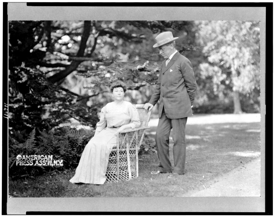 Woodrow Wilson, full-length portrait, standing next to his wife, Ellen, seated in a chair LCCN96520621