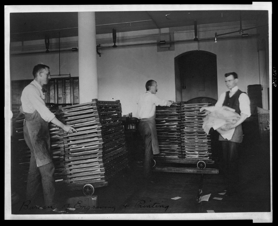 Workers moving newly printed currency into a drying box where sheets will dry before the next wetting and printing at the Bureau of Engraving & Printing LCCN2006692527