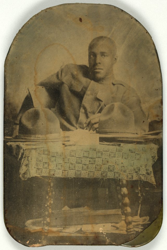 World War I soldier, half-length portrait, seated, facing front, with two hats on table LCCN2002719501