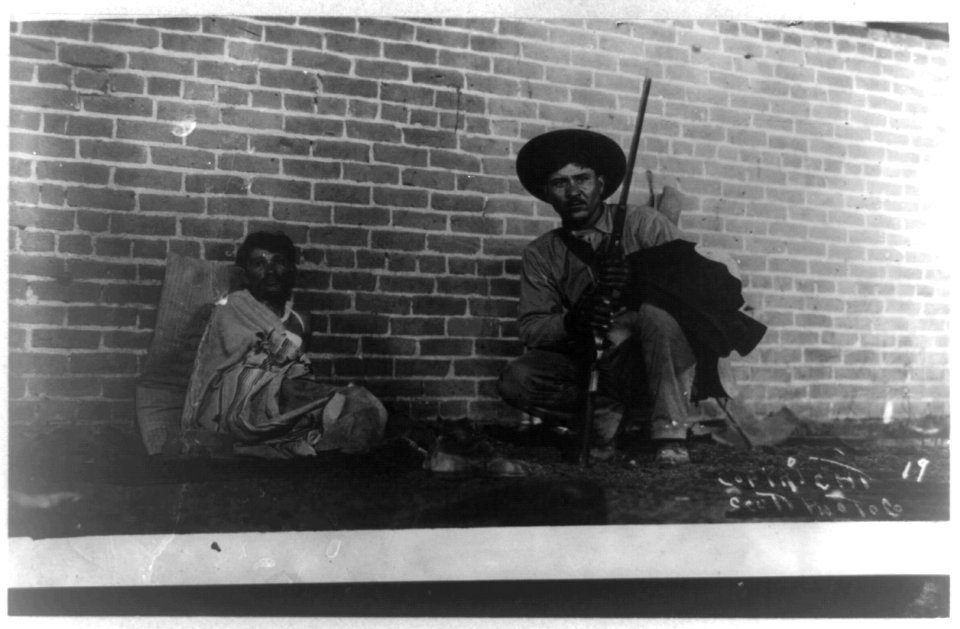 Wounded man and insurrecto with rifle along brick wall LCCN93514463