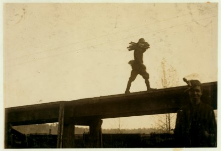 Young boy carrying armful of steel rods, 'spragging irons' along the elevated track at the Bessie Mine. LOC nclc.01095