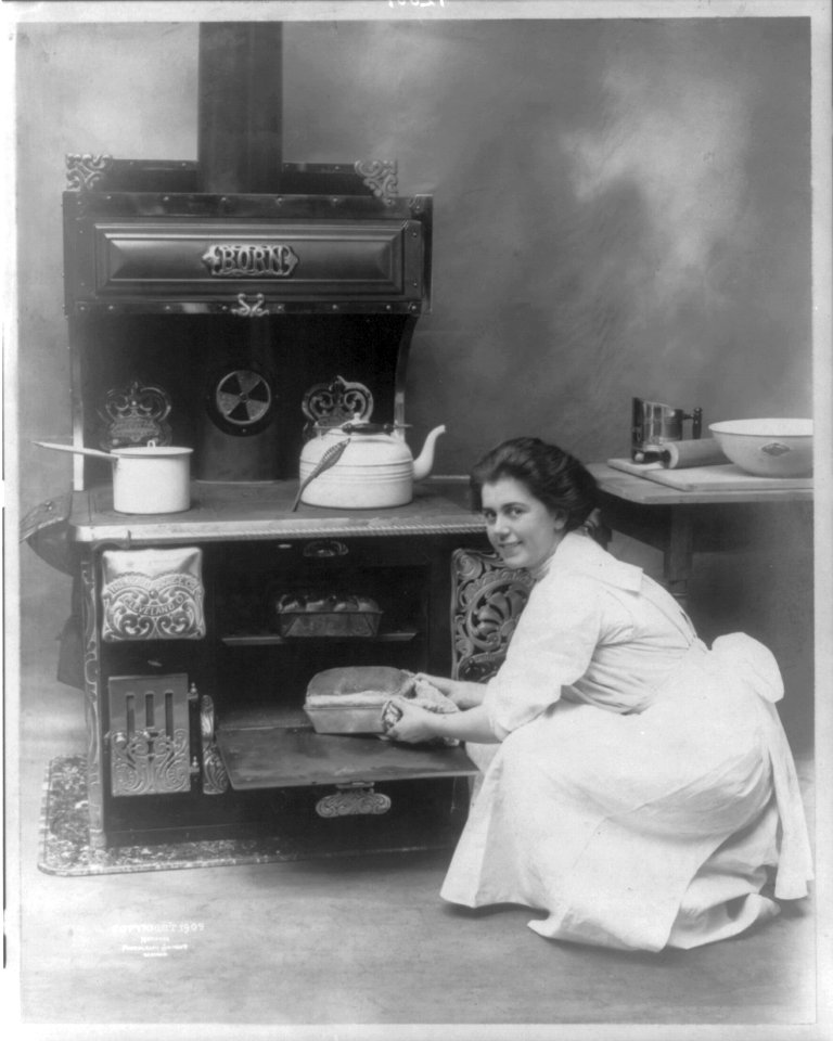 Young woman removing a loaf of bread from an oven made by the Born Range Co. LCCN2011645146