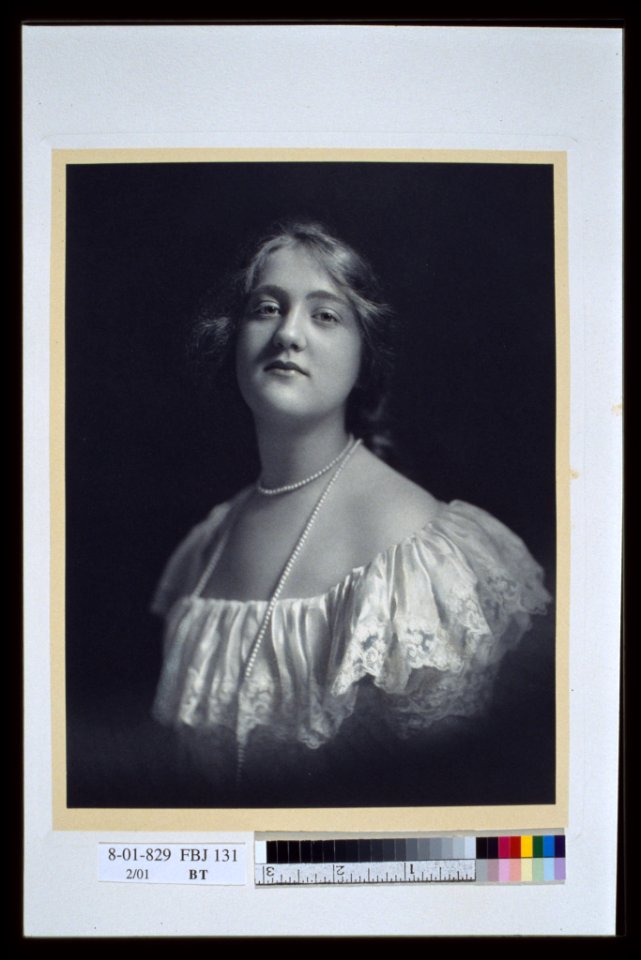 Young woman wearing an off-the-shoulder dress and long pearl necklace, looking front, head-and-shoulders portrait LCCN2004676399