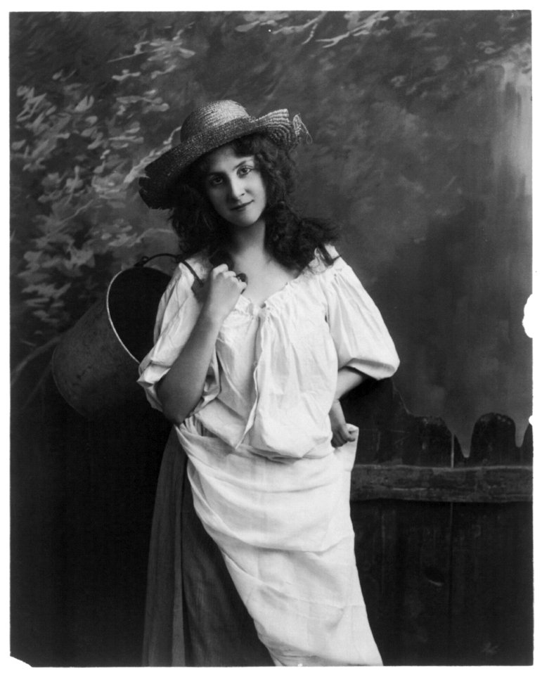 Young women modeling- 3-4 lgth., standing, holding bucket wearing broken straw hat LCCN2003677237