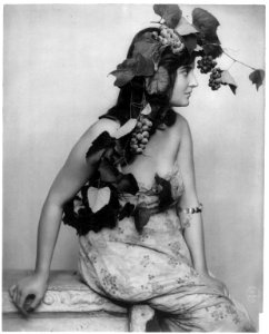 Young woman posed, seated, three-quarters length, facing right; with grapes, vines and leaves draped over head LCCN2005686789