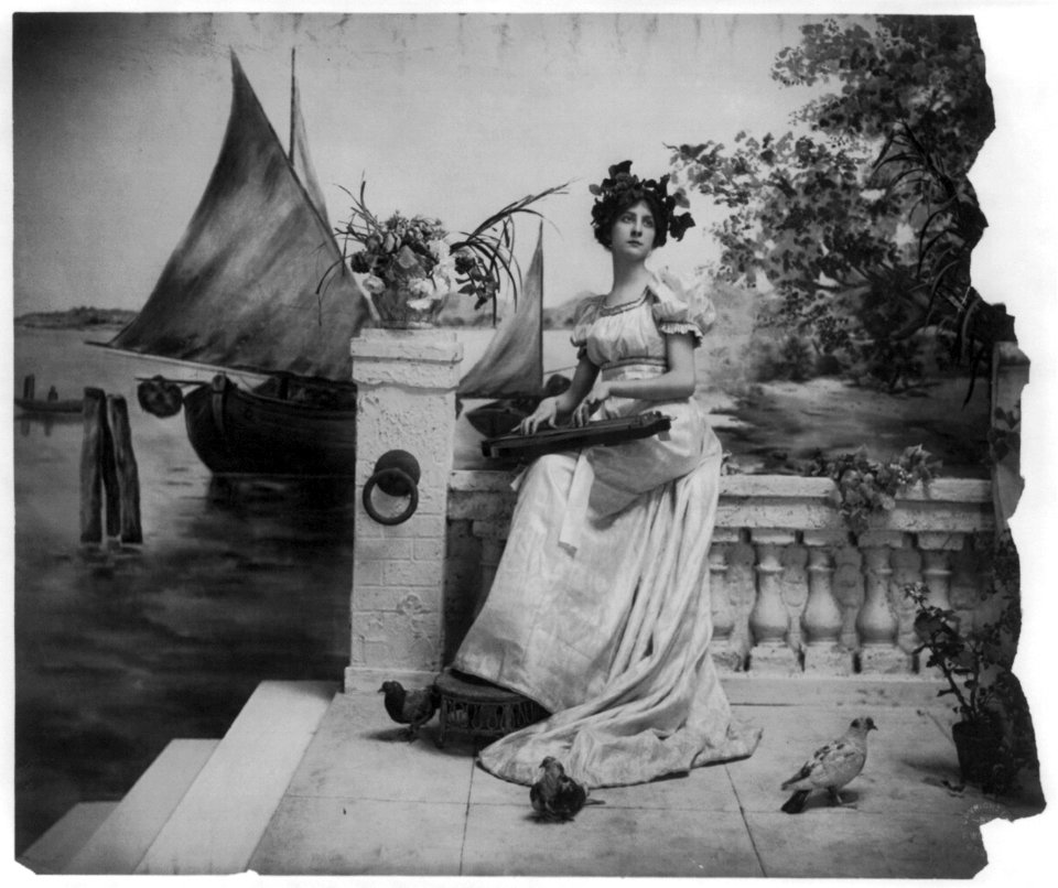 Young woman modeling- Full lgth., leaves on head, seated on sea-wall holding zither LCCN2003677231
