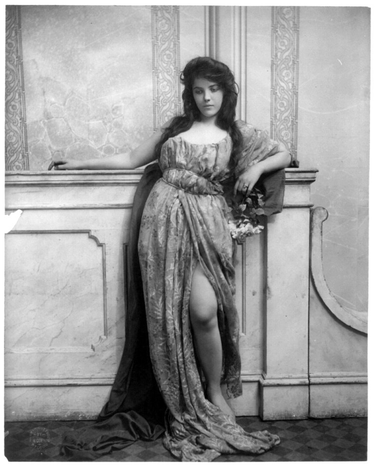 Young woman modeling- full lgth., standing, leaning on mantle and waring split skirt LCCN2003677213