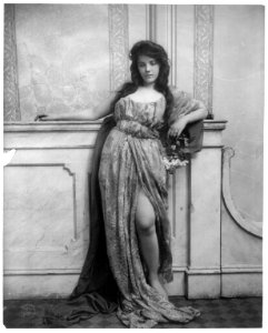 Young woman modeling- full lgth., standing, leaning on mantle and waring split skirt LCCN2003677213