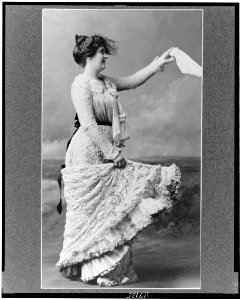 Young woman, full-length portrait, wearing lace dress, standing, facing right, waving handkerchief LCCN97513785
