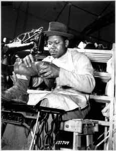 Howard Wilson operating the sewing machine in the C. & E. Shoe Shop at Fort Benning, Georgia, as he finishes off a - NARA - 531138
