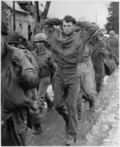 A lanky GI, with hands clasped behind his head, leads a file of American prisoners marching along a road somewhere on... - NARA - 531236 photo