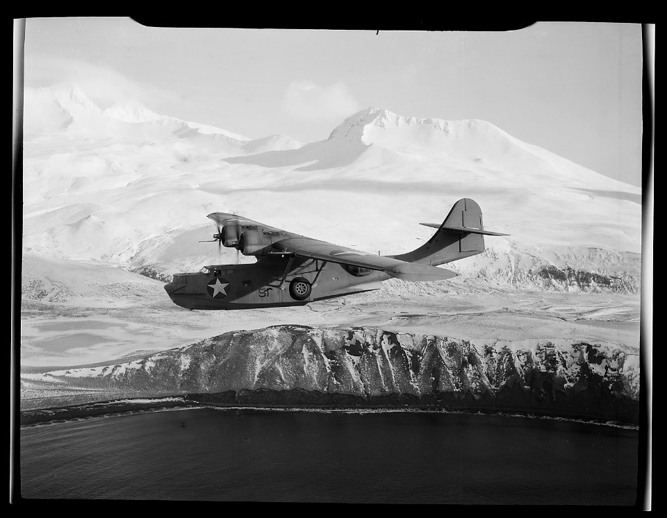 A PBY-5A Catalina patrol bomber cruises against a backdrop of snow-clad mountains in Aleutian Islands, searching for... - NARA - 520976